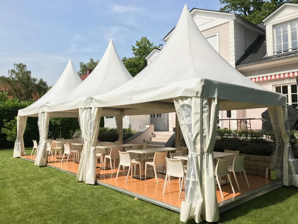 Vogel Event Partner - Zeltpavillons Zeltpavillons mit Holzboden über Tischen und Stühlen in einem Garten.