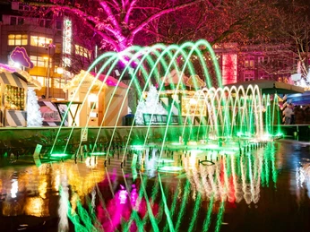 HEAVENUE Cologne Bunte Lichter und Wasserfontänen erhellen den lebhaften Weihnachtsmarkt auf dem Friesenplatz in Köln.Colorful lights and water fountains illuminate the lively Christmas market on Friesenplatz in Cologne.