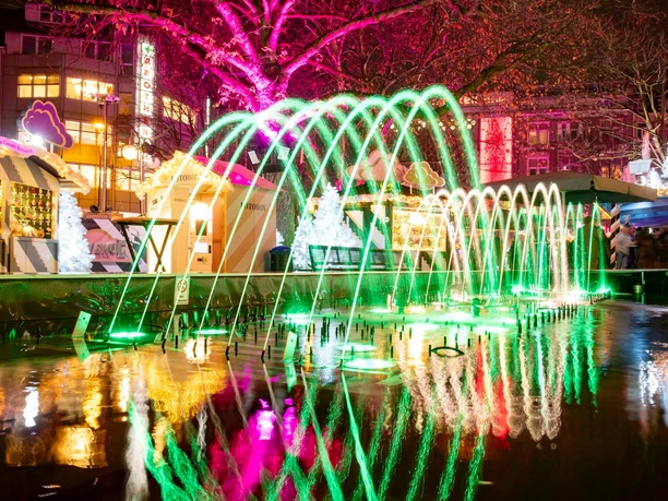 HEAVENUE Cologne Colorful lights and water fountains illuminate the lively Christmas market on Friesenplatz in Cologne.