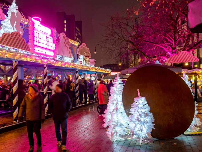 HEAVENUE Cologne Bunt erleuchteter Weihnachtsmarkt mit leuchtenden Engeln und weißen Tannen in der Abenddämmerung.Colorfully illuminated Christmas market with glowing angels and white fir trees at dusk.