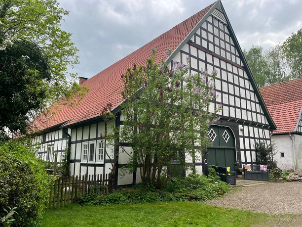 Ferienwohnung "wie bei Muddi" Fachwerkhaus mit rotem Ziegeldach, grüner Scheunentür, blühendem Flieder und kleinem Gartenzaun.