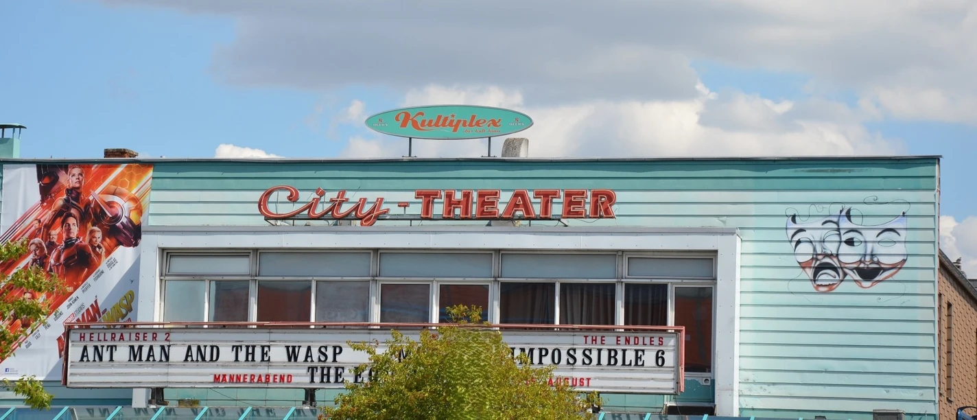 Außenansicht des Kinos Kultiplex City-Theater mit blauer Fassade, Programmtafel und Masken.