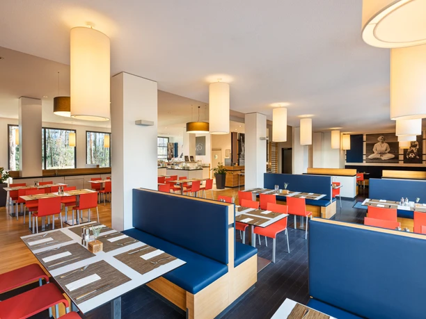 Lindner Hotel Frankfurt Sportpark - Restaurant Helles Restaurant mit blau-orangen Sitzbereichen und modernen Lampen