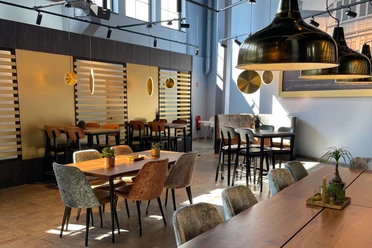 Helles Restaurant mit modernen Holztischen, Polsterstühlen und großen goldfarbenen Lampen.