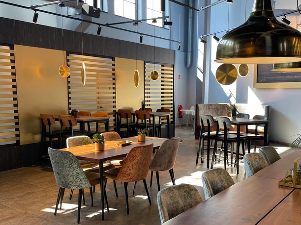 IMG_7300 (c) Kai-Uwe Schulz_Erlebnis Bremerhaven_Ausschnitt.jpg Helles Restaurant mit modernen Holztischen, Polsterstühlen und großen goldfarbenen Lampen.