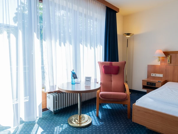 Parkhotel Bad Homburg - Hotelzimmer Helles Zimmer mit Sessel, Tisch und Bett im Parkhotel Bad Homburg..