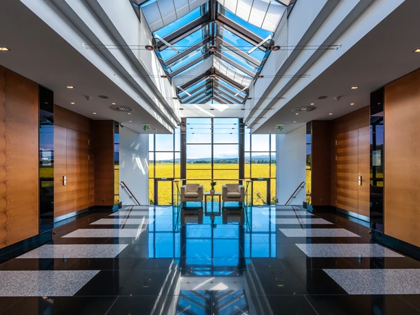 Dorint Hotel Main Taunus Zentrum - Atrium Helles Atrium mit Glasdach, Sitzbereich und Blick auf gelbes Feld