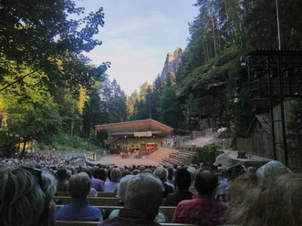 Freilichtbühne im Wald mit Publikum und Bühne bei Dämmerung.