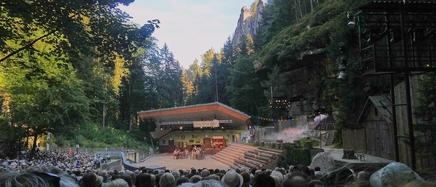 Freilichtbühne im Wald mit Publikum und Bühne bei Dämmerung.