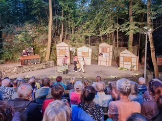 Freilichttheateraufführung im Wald mit Zuschauern und Schauspielern auf der Bühne.