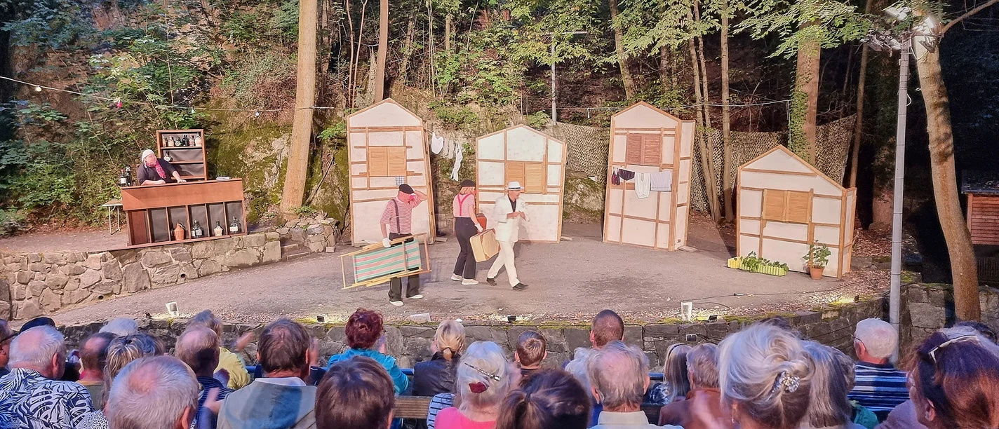 Freilichttheateraufführung im Wald mit Zuschauern und Schauspielern auf der Bühne.