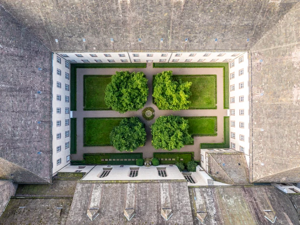 Corvey-Schloß-Corvey-Teutoburger-Wald-Kulturkreis-Hoexter-Corvey-D-Ketz-205-CC-BY-SA.jpg Quadratisch angelegter Innenhof von Schloss Corvey mit symmetrischen Rasenflächen und Bäumen