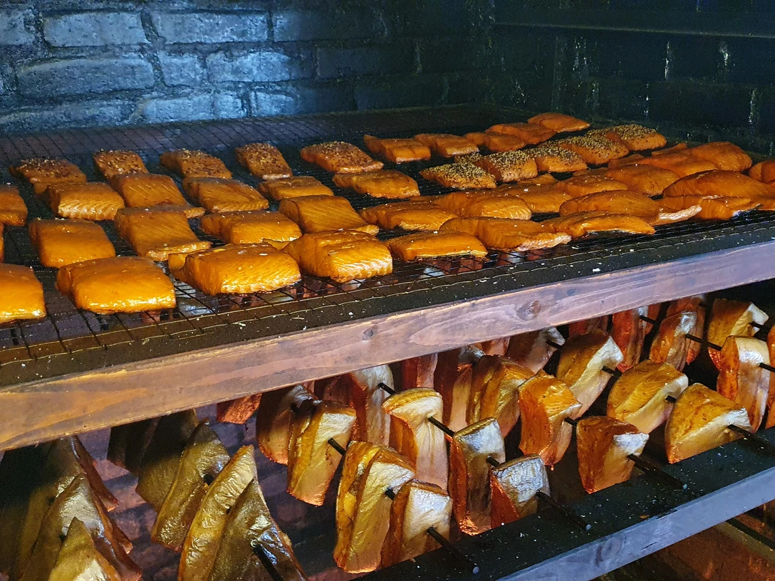 Frisch geräuchert bei Franke 20210422_103330 (c) Tanja Mehl_Erlebnis Bremerhaven GmbH.jpg Räucherofen mit goldbraunen Fischfilets auf Gittern und Holzstücken zum traditionellen Räuchern.