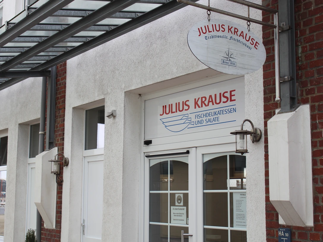 Julius Krause IMG_8179 (c) Jasmin Emilia Meyer_Erlebnis Bremerhaven.JPG Eingang des Fischdelikatessengeschäfts Julius Krause mit Glasvordach und weißer Hausfassade.