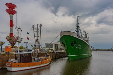 DSC00724 (c) Birgit Hass_Erlebnis Bremerhaven.jpg Krabbenkutter und grünes Schiff im Hafen von Bremerhaven vor grauem Himmel und rotem Leuchtturm