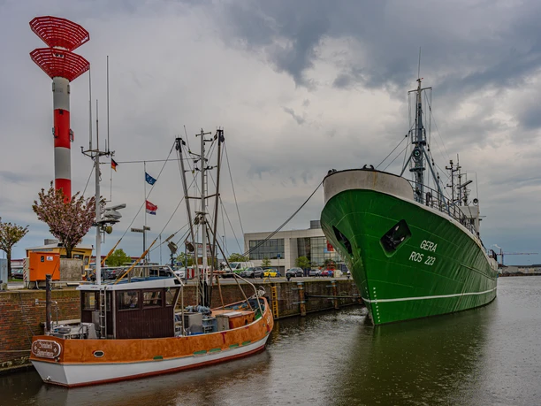 DSC00724 (c) Birgit Hass_Erlebnis Bremerhaven.jpg Krabbenkutter und grünes Schiff im Hafen von Bremerhaven vor grauem Himmel und rotem Leuchtturm