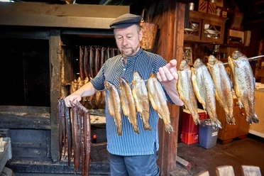 Fischerlebnis DSC_3826 (c) Anna Meurer_Erlebnis Bremerhaven.jpg Fischer in traditioneller Kleidung hält frisch geräucherte Fische und Aale vor der Räucherkammer