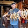 Fischerlebnis DSC_3826 (c) Anna Meurer_Erlebnis Bremerhaven.jpg Fischer in traditioneller Kleidung hält frisch geräucherte Fische und Aale vor der Räucherkammer