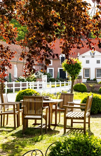 Historisches Landgut mit roten Ziegeldächern, Gartenmöbeln im Grünen und üppiger Bepflanzung.