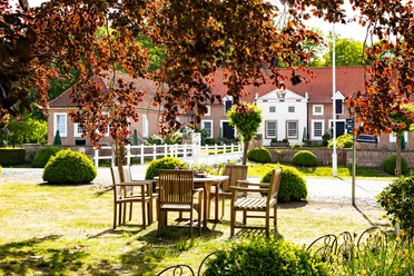 Gut Landegge_5114-HDR.jpg Historisches Landgut mit roten Ziegeldächern, Gartenmöbeln im Grünen und üppiger Bepflanzung.