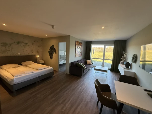 Lichte familiekamer met tweepersoonsbed, bank, eethoek en uitzicht op een weids weidelandschap.