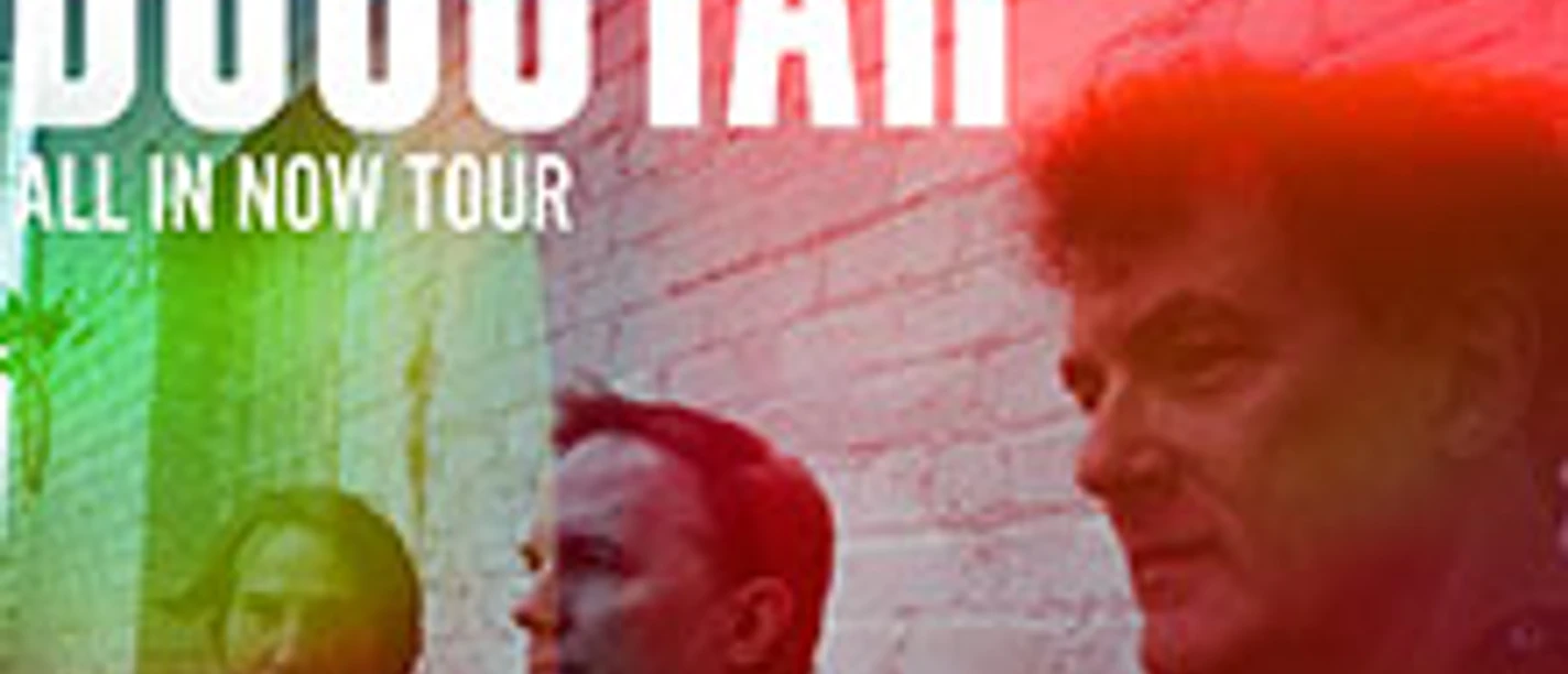 Drei Musiker vor einer Backsteinmauer, beleuchtet von buntem Licht.