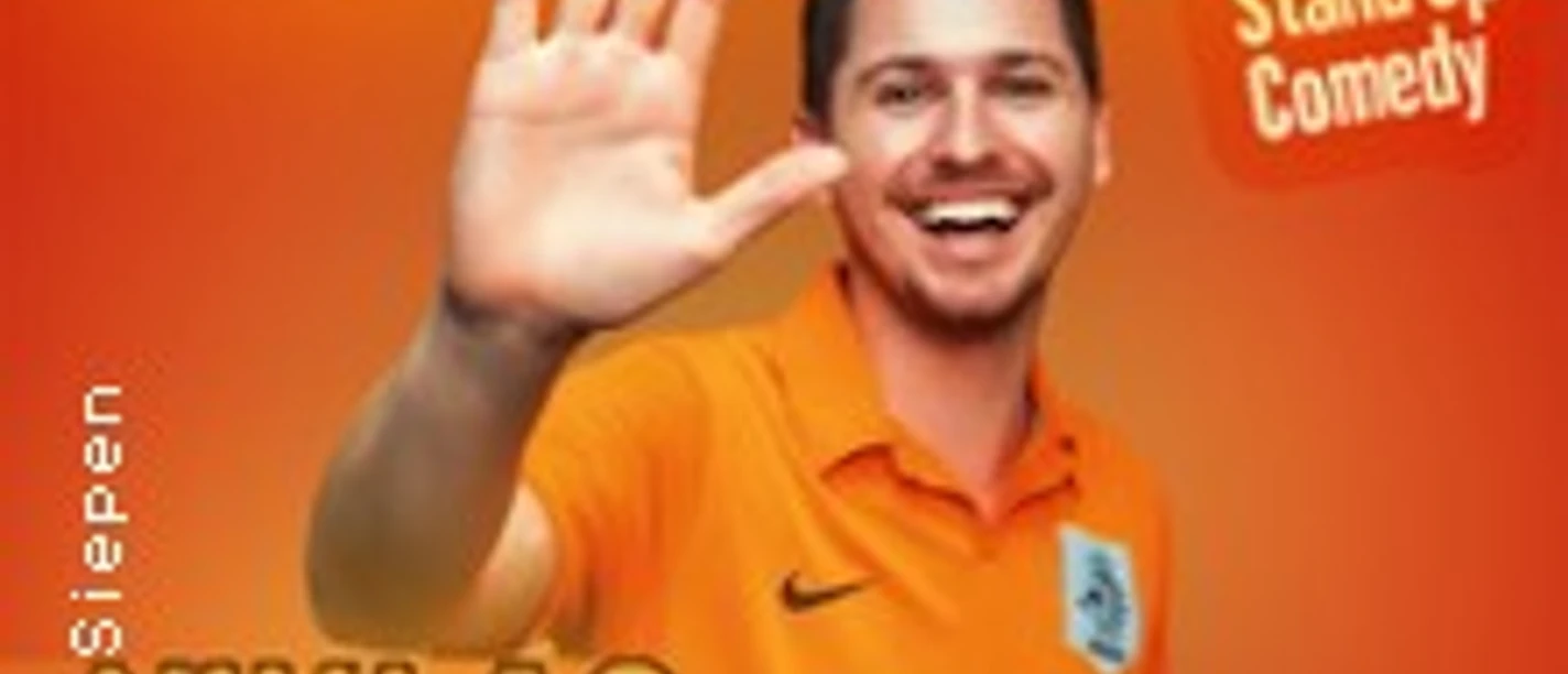 Niklas Siepen lächelt in orangenem Shirt vor orangefarbenem Hintergrund und hebt die Hand zur Begrüßung.