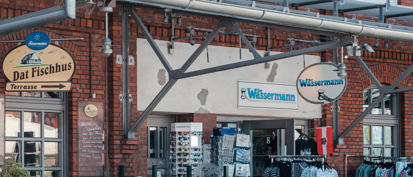 IMG_6499 (c) Nastasia Simms_Erlebnis Bremerhaven_CC BY_NENNUNG DES COPYRIGHTS.jpg Eingang des Geschäfts Der Wassermann in Bremerhaven mit Kleidung, Sonnenbrillen und Postkartenständern.