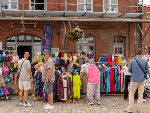 CAL_4834 (c) Carmen Lindemann_Erlebnis Bremerhaven_CC0.jpeg Menschen stöbern vor einem Backsteingebäude durch bunte Kleidung in einem Straßenverkauf.