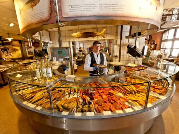 KEY VISUAL 3-Fischmarkt Räucherecke_0092 (c) Fiedler_Erlebnis Bremerhaven.jpg Verkäufer hinter runder Theke mit großer Auswahl an frisch geräuchertem Fisch in Bremerhaven
