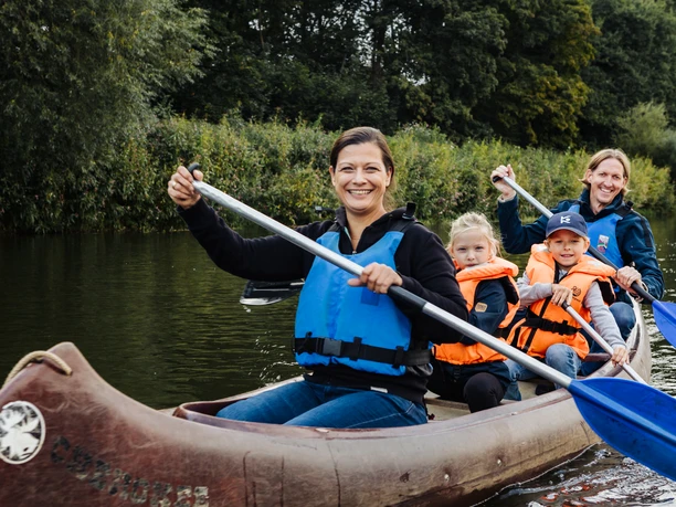 Familienzeit CR Kanu-Camp Lingen.jpg Familie paddelt lachend im Kanu auf der Ems, umgeben von grünem Ufer und ruhigem Wasser