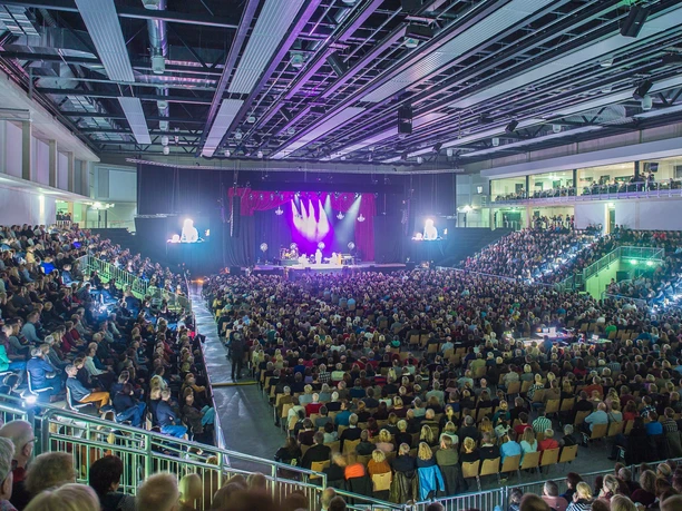 Lingen LIVE3 © Helmut Kramer.jpg Publikum in großer Veranstaltungshalle bei Konzert mit bunter Lichtshow und gefüllten Sitzreihen