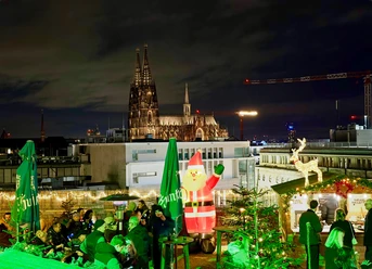 Ein festlich beleuchteter Weihnachtsmarkt auf einer Dachterrasse in Köln mit Blick auf den Dom.