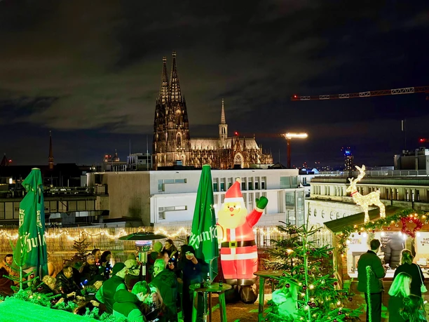Ein festlich beleuchteter Weihnachtsmarkt auf einer Dachterrasse in Köln mit Blick auf den Dom.