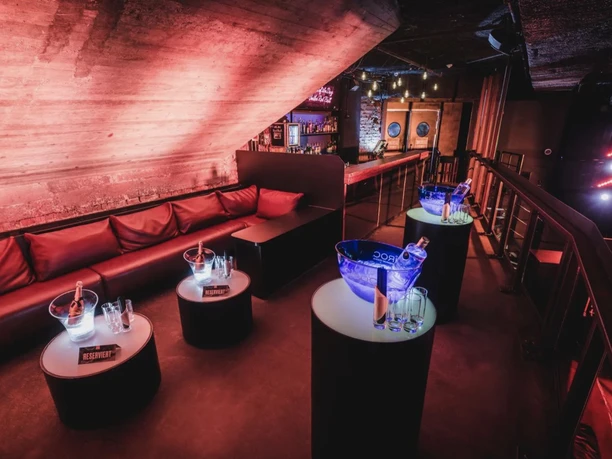 Gibson Club - Lounge Lounge-Eck mit einer roten Couch, kleinen Tischen und Stehtischen mit Getränken