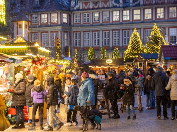 WF-Weihnachtsmarkt-12.jpg Menschen flanieren über den festlich beleuchteten Weihnachtsmarkt in Wolfenbüttel im Schneefall.