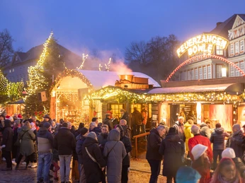 WF-Weihnachtsmarkt-Feuerzangenbowle 03.jpg Abendlicher Weihnachtsmarkt in Wolfenbüttel mit Lichterketten, Holzbuden und Besuchern bei Feuerzangenbowle