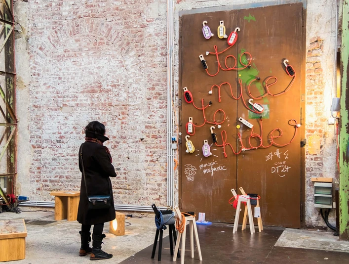 PASSAGEN - Interior Design Days Cologne Eine Kunstinstallation auf einer industriellen Backsteinmauer. Eine Person betrachtet mit Interesse eine verschlossene Tür, die mit farbenfrohen, kreativen Graffiti verziert ist.An art installation on an industrial brick wall. A person looks with interest at a locked door decorated with colorful, creative graffiti.