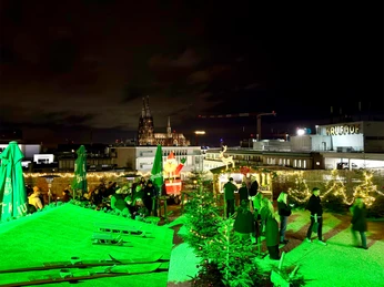 Kölns höchster Weihnachtsmarkt auf der SonnenscheinEtage Nächtlicher Weihnachtsmarkt auf der Dachterrasse mit grünem Licht und Kölner Dom im Hintergrund.Christmas market at night on the roof terrace with green light and Cologne Cathedral in the background.