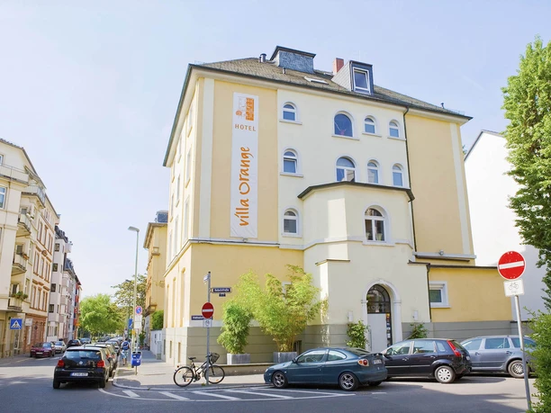 Villa Orange - Außenansicht des Hotels Villa Orange Außenansicht des gelben Hotels Villa Orange an der Straßenecke.