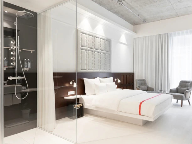 Ruby Louise Hotel Frankfurt - Rooms Hotel room with a white bed, two gray armchairs and a glass shower