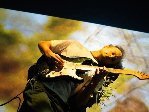Ein Mensch liegt auf dem Boden und spielt dabei eine elektrische Gitarre.