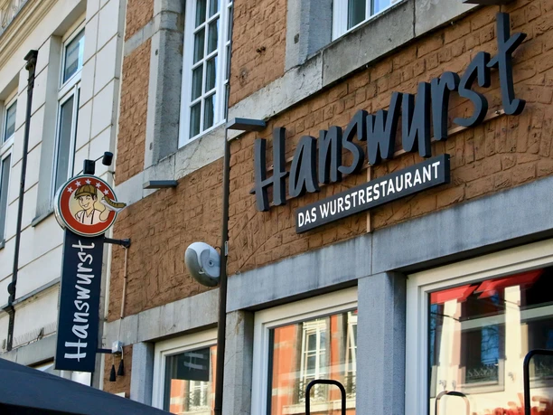Hanswurst (c) Steve Cozort (2).jpg Außenfassade des Restaurants "Hanswurst" mit Wandschild und großer Schrift des Namens.