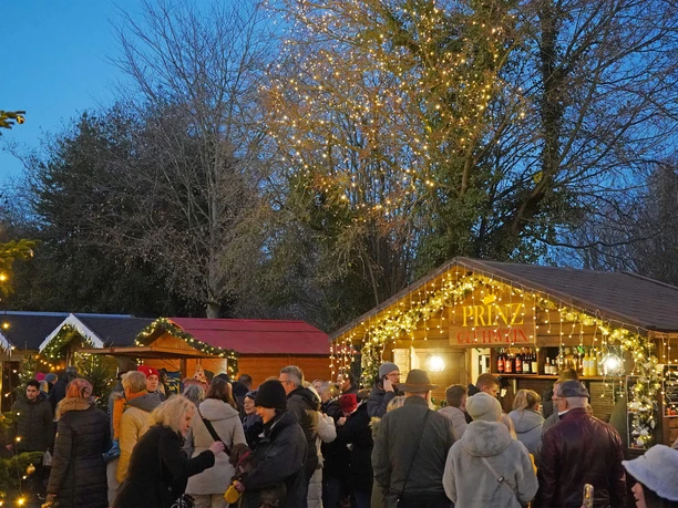 Menschen bummeln abends über den festlich beleuchteten Weihnachtsmarkt in Bad Zwischenahn.