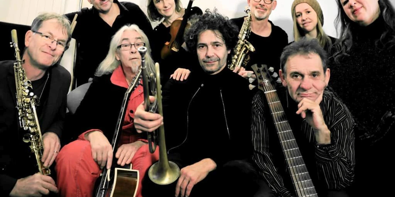 Art'n Schutz Orchester (c) Loni Liebermann.jpg Eine Gruppe dunkel gekleideter Personen steht und hockt mit ihren verschiedenen Instrumenten in der Hand.