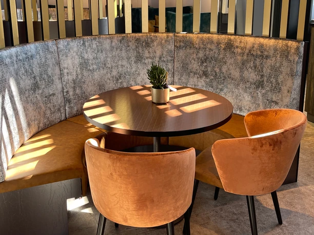 IMG_7302 (c) Kai-Uwe Schulz_Erlebnis Bremerhaven_Ausschnitt.jpg Runder Holztisch mit zwei Samtsesseln und gepolsterter Sitzecke in warmem Sonnenlicht.