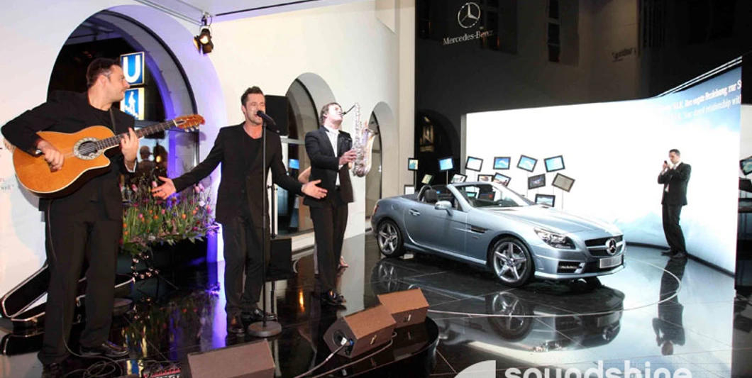 Messeband, Livekünstler, Standparty.jpg Ein Sänger, ein Gitarrist und ein Saxophonist sorgen für musikalischer Untermalung auf einer AutoausstellungA singer, a guitarist and a saxophonist provide background music at a car exhibition