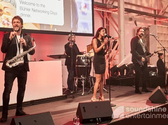 Soundshine Live Band, Eventband, Galaband.jpg Eine Band bestehend aus einer Sängerin, Gitarristen, Saxophonisten und Schlagzeuger stehen auf einer BühneA band consisting of a singer, guitarist, saxophonist and drummer stand on one stage