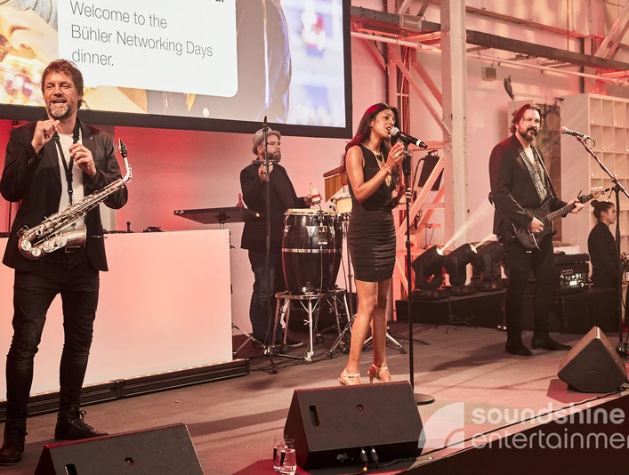 Soundshine Live Band, Eventband, Galaband.jpg Eine Band bestehend aus einer Sängerin, Gitarristen, Saxophonisten und Schlagzeuger stehen auf einer BühneA band consisting of a singer, guitarist, saxophonist and drummer stand on one stage