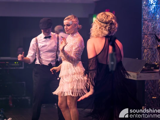 Soundshine Band 20s.jpg Zwei Frauen und ein Mann tanzen im 20er Jahre Stil gekleidet auf der BühneTwo women and a man dressed in 1920s style dance on stage
